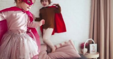 Mutlu çocuklar, süper kahraman kılığındaki kardeşler eğleniyorlar, güneşli bir günde yatakta zıplıyorlar.