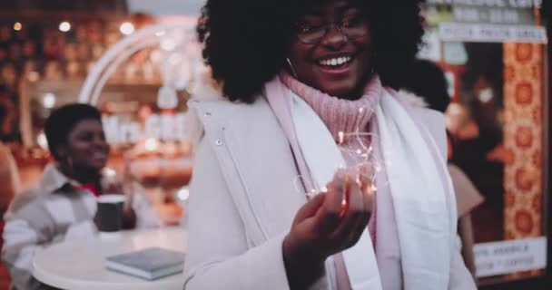 光のガーランドを持つ幸せな若い女性冬休みのクリスマスマーケットで楽しんで — ストック動画