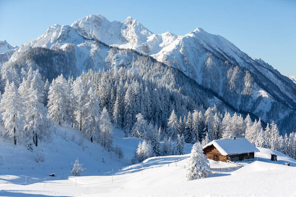 Зимний фон природы. Снежный пейзаж с традиционной деревянной хижиной и горами на заднем плане.