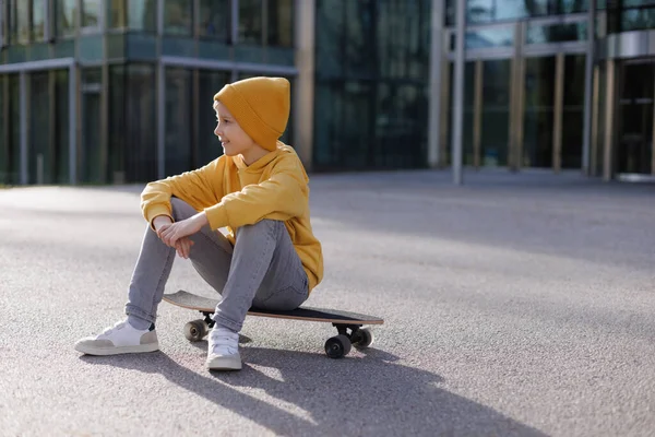 Foto de niño patinador europeo en ropa casual sentado en su monopatín —  Fotos de Stock