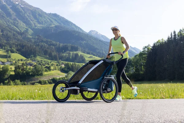 Mother running in an alpine terrain using a jogging stroller. High quality photo