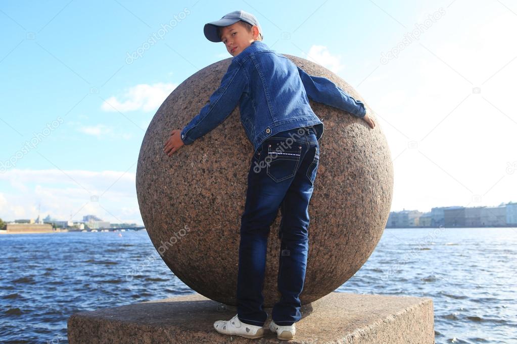 Boy hugging granite ball on the Neva River in St. Petersburg