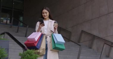 Alışveriş merkezinin yanında çantaları olan bir kadın cep telefonu kullanıyor.