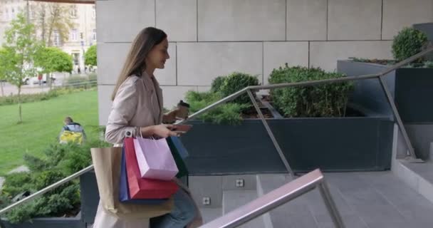 Жінка ходить по сходах з мобільними та торговими сумками — стокове відео
