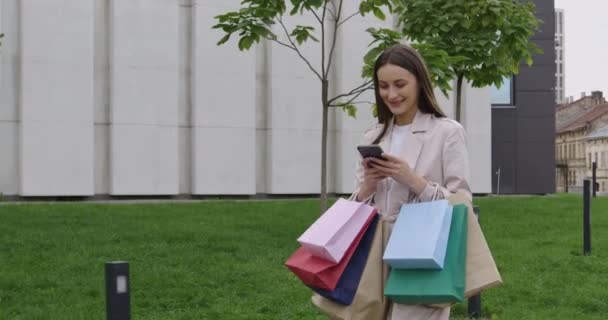 Mujer atractiva que lleva bolsas de compras y el uso de móviles — Vídeos de Stock