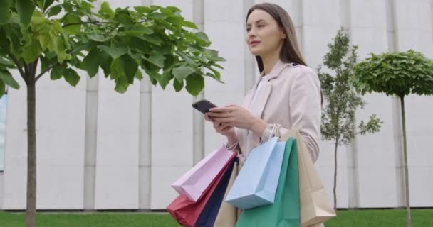 Nő használ mobil szabadban bevásárló táskák a kezében — Stock videók