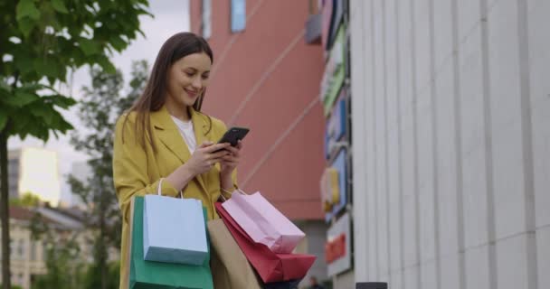 쇼핑 센터 근처에서 스마트폰을 사용하는 가방을 든 여자 — 비디오