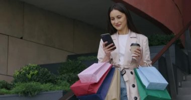 Cep telefonu kullanan ve alışveriş merkezinin yakınında kahve içen bir kadın.