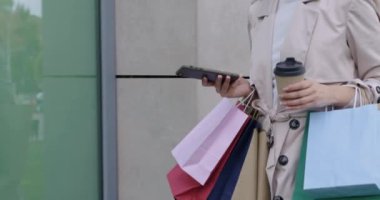 Alışveriş sonrası çanta taşıyan ve cep telefonu kullanan bir kadın.