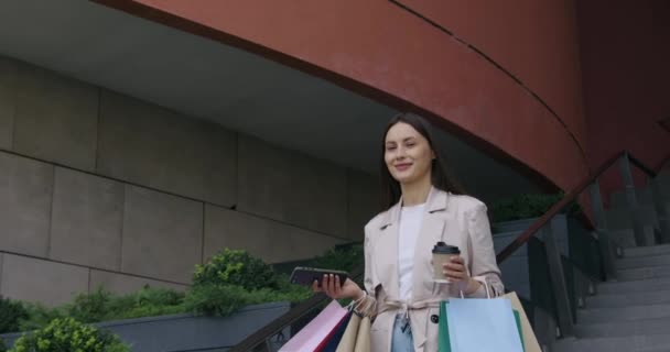 Happy brunette with bags and mobile walking near mall — Stock Video