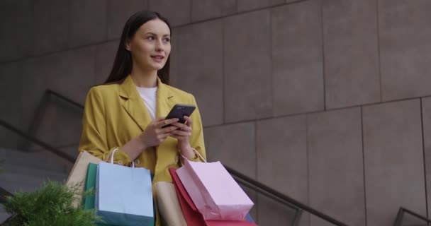 Senhora usando móvel enquanto está com sacos de compras ao ar livre — Vídeo de Stock