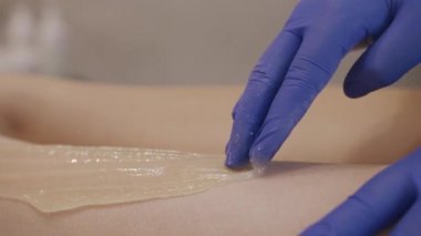 Cosmetologist doing sugaring procedure for female client
