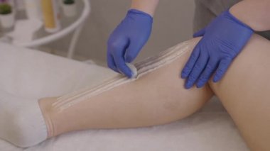 Cosmetologist in gloves waxing female legs