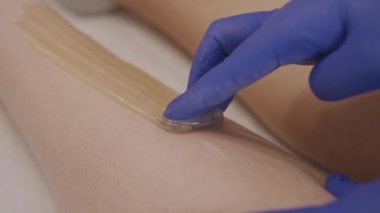 Cosmetologist epilating woman legs using sugaring technique
