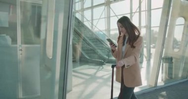 Havalimanı yakınlarında çantasıyla dolaşan şık bir iş kadını ve modern akıllı telefon kullanıyor. Seyahatten önce başarılı kadın girişimci sorunları çözüyor.