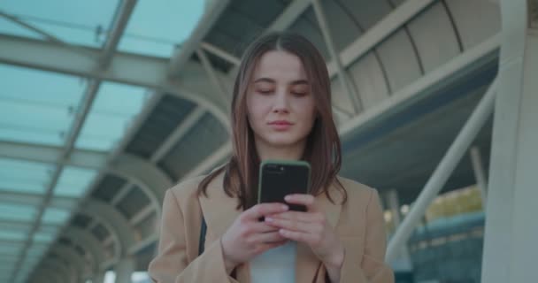 モバイル画面を見ながら笑顔の魅力的なビジネス女性の肖像画。手にスマートフォンで路上に立っている正式な服でかなり暗い髪の女性. — ストック動画