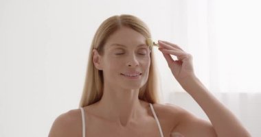 Gorgeous woman massaging face skin using facial trendy jade quartz roller device for detox of perfect skin. Spa technique skincare ads concept 