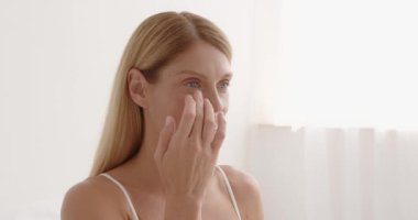 Smiling senior woman applying anti-aging lotion to remove dark circles under eyes. Happy mature woman using cosmetic cream to hide wrinkles below eyes. Lady using day moisturiser 