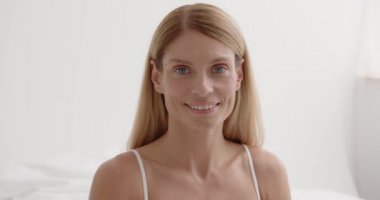 Aged Beauty. Portrait of attractive nude mature lady with smooth skin smiling to camera, posing over light bedroom background