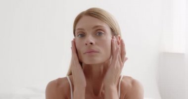 Closeup face of mature woman with wrinkles massaging face at home. Senior woman touching her perfect skin and looking at camera. Aging process concept 
