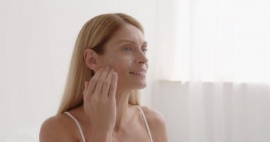 Mature female model with cosmetic product. Close up shot of middle aged beautiful woman applies anti aging cream on face undergoes beauty treatments cares about skin poses against white background 