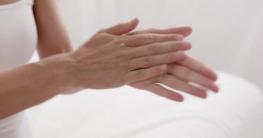 Middle age woman pouring cream on hand sitting on bed at bedroom closeup. Lady spending morning alone. Cosmetics, moisturising skin, body care at home concept 