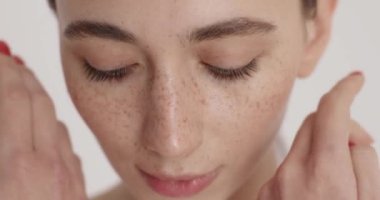 Sensual young woman gently touching her smooth healthy skin on face after hydrating routine. Close up of natural beauty of female model. Skin care and treatment concept