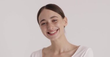 Adorable young woman with a beaming smile showing her soft skin while posing over white background. Beauty fashion model with perfect skin and nude makeup. Woman appearance concept