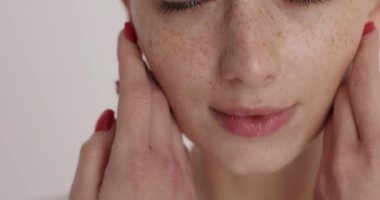 Close up portrait of pretty woman with red manicure touching gently her face while enjoying skin after moisturising. Beautiful young model with freckles and natural beauty