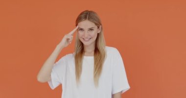 Responsible blond woman holding hand near head saluting, patriotic gesture, honour and dignity. Indoor studio shot isolated on orange background 