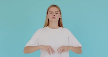 Blond woman closing eyes and holding hands up in mudra gesture, meditating, yoga exercise to reduce stress. Indoor studio shot isolated on blue background 