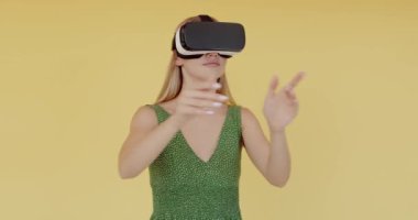 Amazed teen student girl using headset helmet app to play simulation game. Young woman in VR goggles isolated on yellow background. Addiction from technology concept 