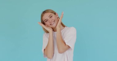 Portrait of happiness woman looking at camera with toothy smile from her palms. Studio shot, isolated on blue background 