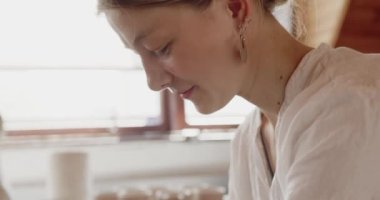 Woman making plate on pottery wheel. Potter shapes the clay product with professional tools. Small business owner working in workshop 