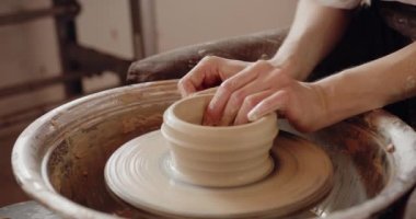 Close-up of potters hands covered with clay making beautiful ware on throwing wheel in pottery workshop. Creativity and traditional crafts concept. 
