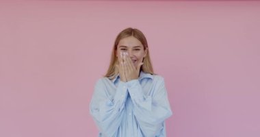 Portrait of happy teenager girl touching face with hands and sincerely smiling, optimistic mood. Indoor studio shot, isolated on pink background 