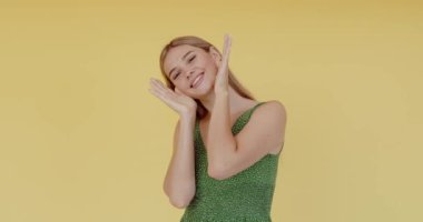 Genç, komik, güzel bir kadın elleriyle yüzünü gizliyor ve gülümsüyor. Mutluyum, gülüyorum. Sarı arka planda izole edilmiş olumlu duygularla yüzünü göster. 