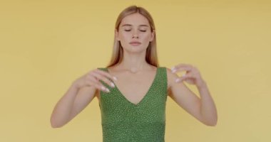Barışçıl, hoş bir kadın, sıradan bir tişört giyiyor, Mudra jestinde parmaklarını tutuyor ve gözleri kapalı meditasyon yapıyor, yoga yapıyor. Sarı arka planda kapalı stüdyo çekimleri 