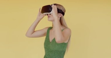 Sarı arka planda sanal gerçeklik gözlüğü takan genç bir kadın. Sanal gerçeklik gözlüğü takan akıllı telefon. Teknoloji, simülasyon, yüksek teknoloji, video oyunu konsepti 