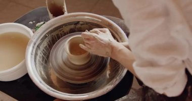 Cropped view of the female making clay pot on the ceramic wheel. Pottery girl is engaged in sculpting. Handicraft production, clay work concept 