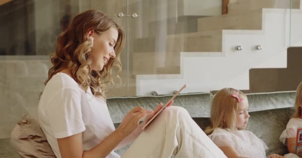 Vista Lateral Mujer Positiva Leyendo Tableta Desplazamiento Mientras Sus Niñas — Vídeo de stock