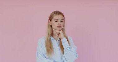 Yukarı bakan mutlu genç bir kadın, kameraya gülümseyerek bakıyor, yeni harika bir fikri var, mavi gömlek giyiyor. Pembe arka planda kapalı stüdyo çekimleri 