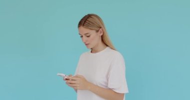 Cep telefonunda mesaj yazan, sosyal ağda yazı okuyan, internette ciddi bir ifadeyle sohbet eden bir kadının portresi. Mavi arka planda kapalı stüdyo çekimi 