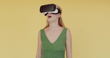 VR gözlüklü genç bir kadın sarı arka planda izole edilmiş elleri işaret ediyor. Artırılmış gerçeklik gözlüklerini test eden kadın. 
