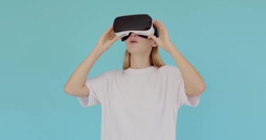 Sarışın kız, simülasyon gerçekçi oyunu oynamak için kulaklık uygulaması kullanıyor. Sanal gerçeklik videosu izliyorum. VR gözlüklü genç kız mavi stüdyo arka planında izole edilmiş. 