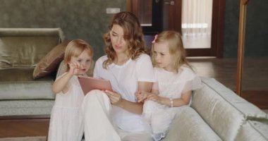 Genç anne ve kızlarından oluşan mutlu bir aile tablet bilgisayarda çizgi film seyrediyor. Oturma odasındaki kanepede otururken kucaklaşıyorlar.