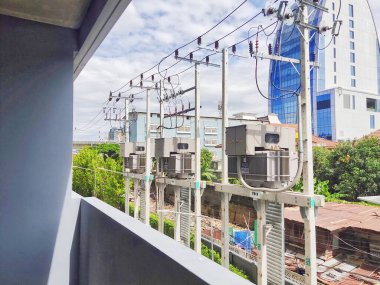 Elektrik trafosu, şehirde yüksek voltajlı güç transformatörü eski ahşap evin arka planına sahip.