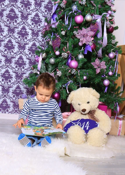 Menino e urso lendo um livro sob a árvore de Natal — Fotografia de Stock