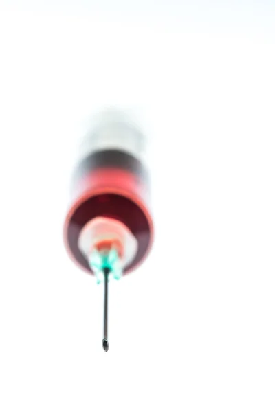 Needle bevel with defocused syringe containing red liquid behind — Stock Photo, Image