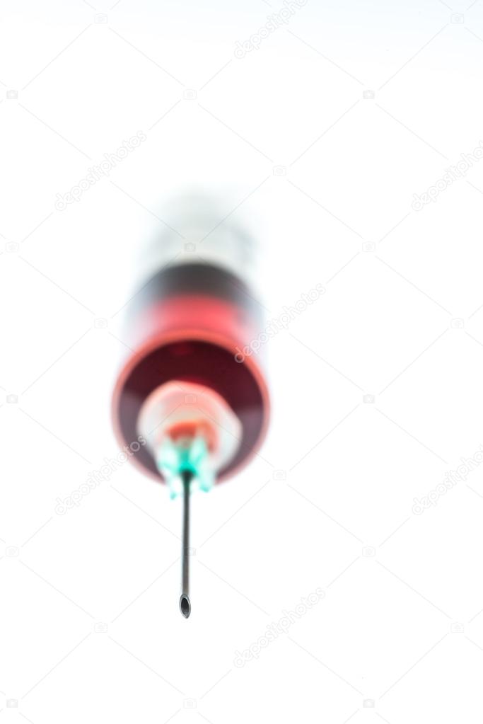 Needle bevel with defocused syringe containing red liquid behind